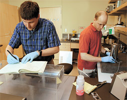 Senior research associate Stefan Turneaure (left) makes a calculation on one project, while graduate student Seth Root determines if his projectile is perfectly cylindrical for another.
