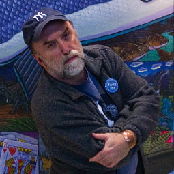 Ray Troll stands in front of <em>Kings</em>, a mural that he painted in 1998 for the lunchroom at Ketchikan High School.
