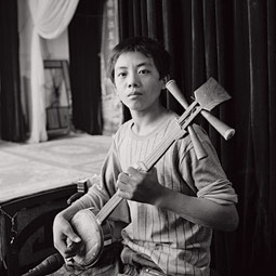 The performers are usually accompanied by a small group of musicians. Here a boy plays a sanxian, a traditional three-stringed instrument.